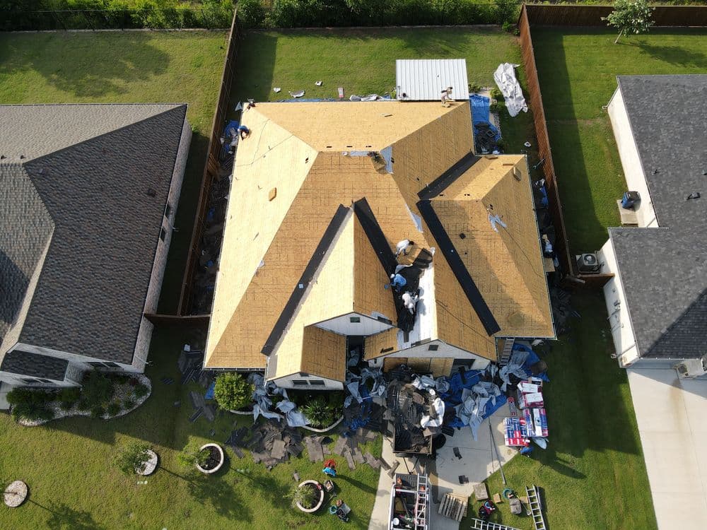 Aerial view of a house undergoing roof replacement with construction materials scattered around.