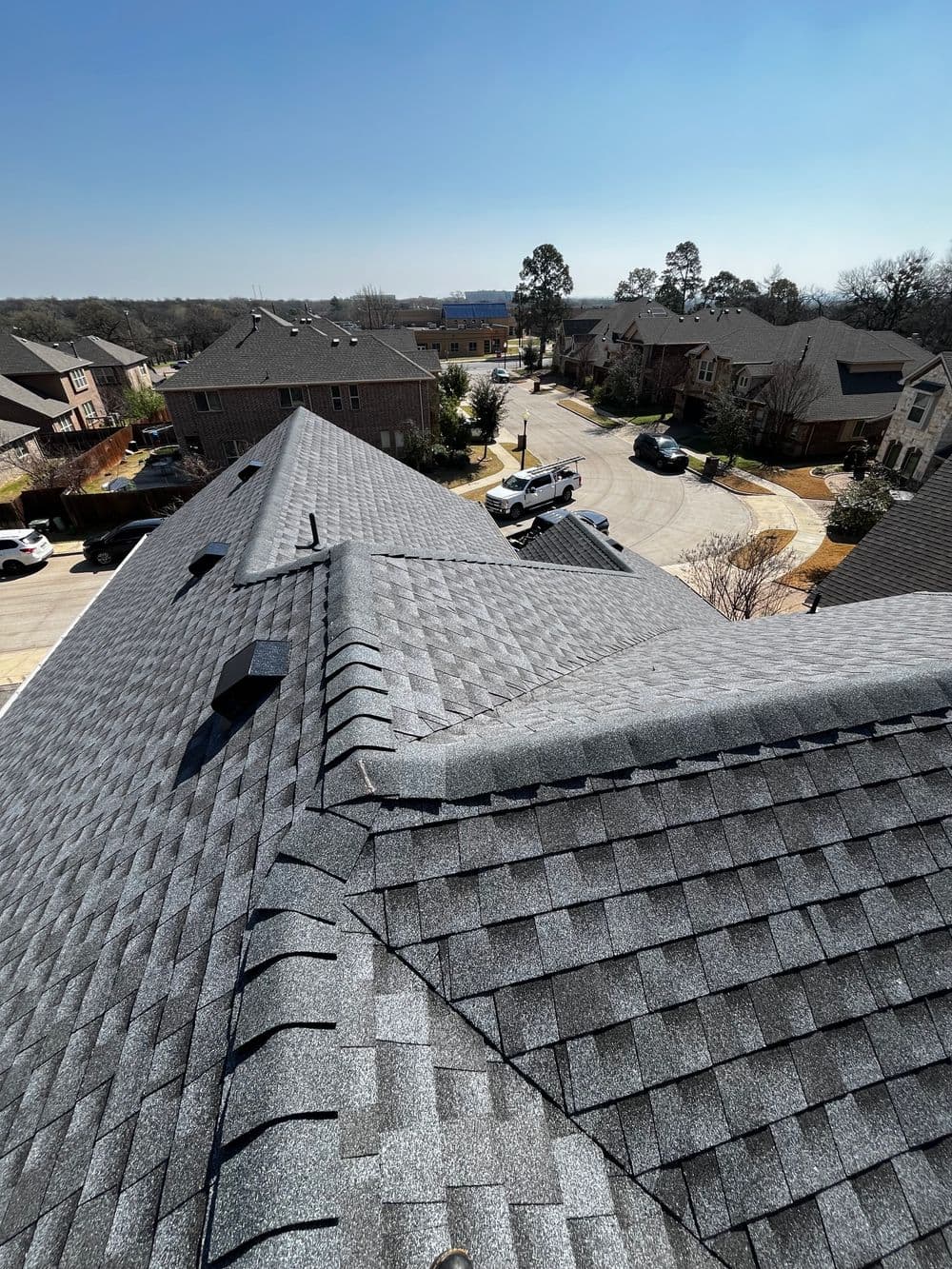 Aerial view of residential roofs with shingle roofing under a clear blue sky.